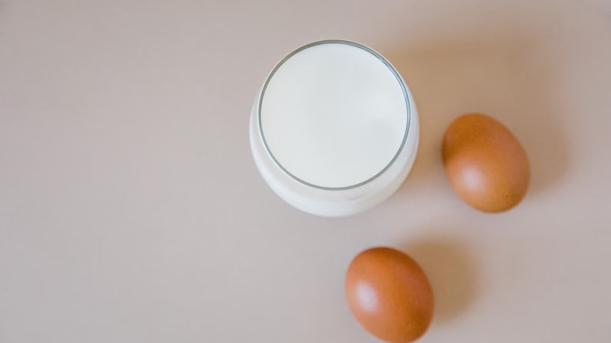 Aesthetic flatlay featuring a glass of milk and two brown eggs on a light surface.